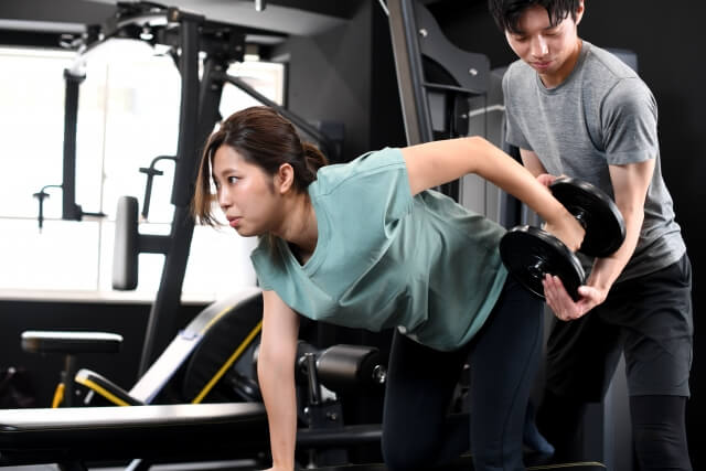 筋トレをする女性と補助する男性トレーナー