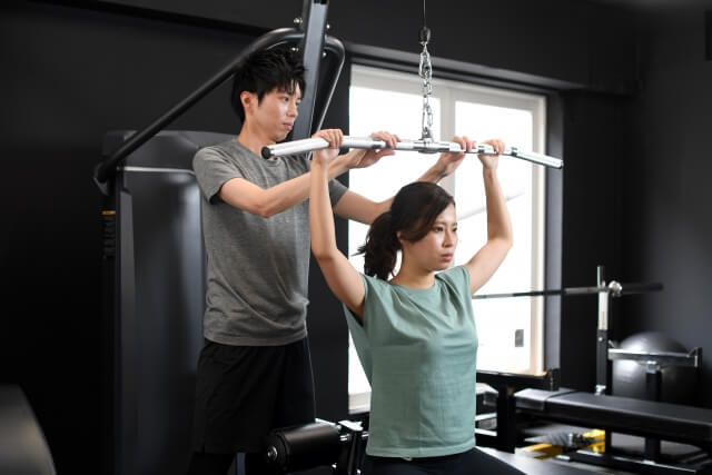 ラットプルダウン中の女性と補助する男性